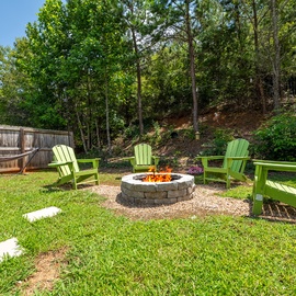 Gather around the fire pit in your private backyard, surrounded by lush trees and vibrant green seating. Perfect for evening s'mores and unwinding under the stars.