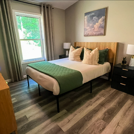 Your peaceful bedroom features a plush bed with fresh linens, warm natural light from the window, and modern touches like a flat-screen TV—perfect for unwinding after exploring.