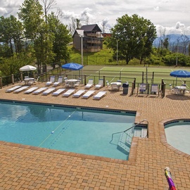 Community outdoor pool and hot tub area with mountain views, surrounded by wooded grounds and recreational facilities.