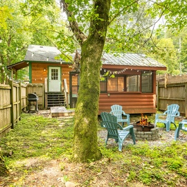 (Grill is no longer available) A peaceful retreat nestled in nature, featuring a fire pit and cozy seating surrounded by towering trees and lush greenery.