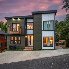 Modern two-story home featuring contemporary architecture and warm interior lighting, set in a peaceful residential neighborhood beneath a vibrant dusk sky.