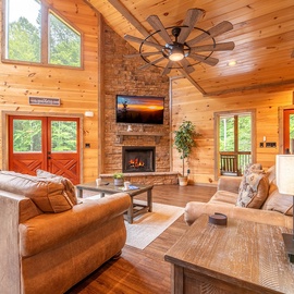 Curl up in this warm, wood-lined living room where the stone fireplace glows and soaring ceilings create a welcoming sense of space. Your mountain escape awaits.