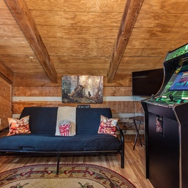 Your personal game room awaits with a classic arcade machine and futon, all framed by cozy wood-beamed ceilings—perfect for unwinding after a day of adventure.