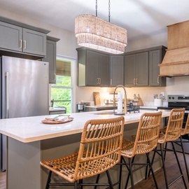 Step into your fully equipped kitchen, where sleek gray cabinetry meets warm wood accents and a spacious island invites you to gather with friends over coffee or cocktails.