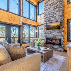 Cozy up in this stunning living room with soaring windows, crackling fireplace, and warm wood details perfect for your mountain getaway.
