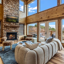 Sink into plush seating by your crackling fireplace, where soaring windows frame peaceful views and warm wood embraces you in comfort.