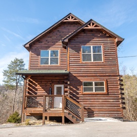 Rustic log cabin exterior nestled among mountain trees with wooden deck and charming architectural details.