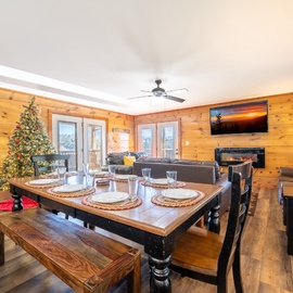 Gather around the rustic dining table where warm wood walls and a crackling fireplace create the perfect atmosphere for memorable meals together.