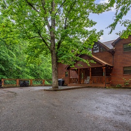 A handsome log cabin nestled among mature trees with a welcoming covered porch and plenty of parking space for arrival.