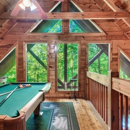 Challenge your family to pool games in this stunning loft space, where towering windows frame forest views and rustic wood creates pure mountain magic.