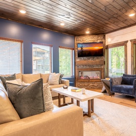 Sink into plush seating and let your worries fade as you gaze at lush greenery through large windows, while the cozy fireplace creates a warm, inviting glow perfect for relaxation.