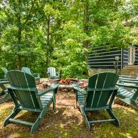 A secluded outdoor fire pit surrounded by Adirondack chairs, nestled among lush trees and natural greenery—perfect for peaceful evenings under the forest canopy.