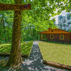 A charming log cabin retreat nestled in the forest awaits, with a welcoming wooden sign marking your arrival to this peaceful woodland escape.