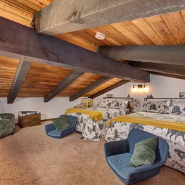 Cozy loft bedroom with rustic exposed beams where you'll sleep peacefully in comfortable beds with charming mountain-themed bedding and plush seating.