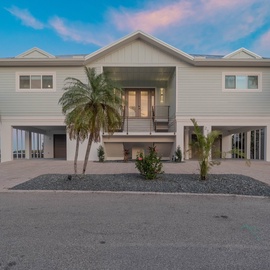 Modern beachside home featuring elevated design with palm trees and tropical landscaping in a serene coastal setting.