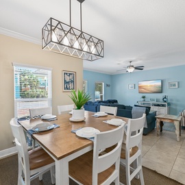 Gather around your elegant dining table beneath the striking geometric chandelier, where coastal blues and warm tones create the perfect atmosphere for memorable meals.