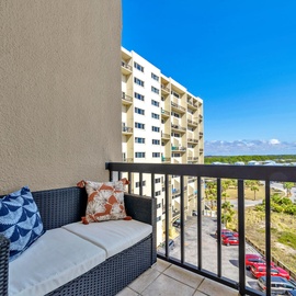 Relax on your private balcony off the primary bedroom with tropical-patterned cushions while enjoying sweeping views of the coastline and neighboring buildings.