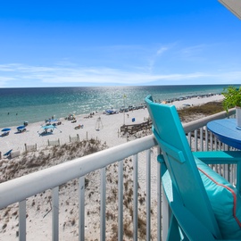 Relax on your private balcony with stunning ocean views, where turquoise chairs invite you to unwind while watching beachgoers below.