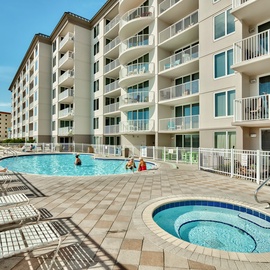 Modern beachfront resort featuring expansive swimming pool and hot tub area surrounded by comfortable loungers and multi-story accommodations.