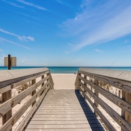 Wooden boardwalk leads across pristine white sand dunes to turquoise waters and endless blue sky.