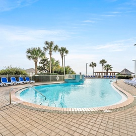 Coastal pool area with palm trees and beachfront building views creating a tropical resort atmosphere.