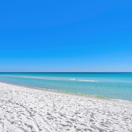 Pristine white sand beach with crystal-clear turquoise waters stretching endlessly under brilliant blue skies.