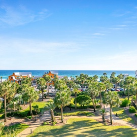 Elevated view showcasing the coastal location with palm trees, nearby buildings, and ocean access in the surrounding area.