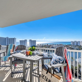 Your private balcony offers stunning coastal views while you dine al fresco at the outdoor table, watching the waves dance beyond the city skyline.