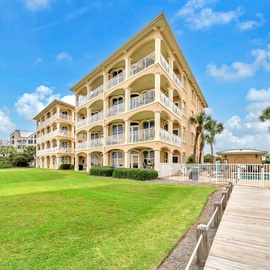 Elegant beachfront resort building with multiple balconies overlooking manicured grounds and palm-lined surroundings.