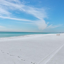 Pristine white sand beach stretches along turquoise waters under bright blue skies, offering a perfect coastal retreat.