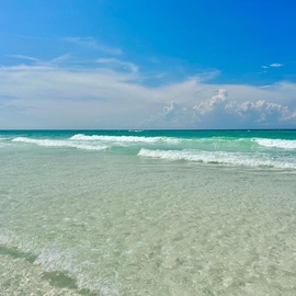 Just steps to the pristine beach with crystal-clear turquoise waters and gentle waves under a brilliant blue sky dotted with fluffy white clouds.