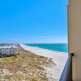 Expansive beachfront stretches along turquoise waters with white sand and coastal homes dotting the shoreline under brilliant blue skies.