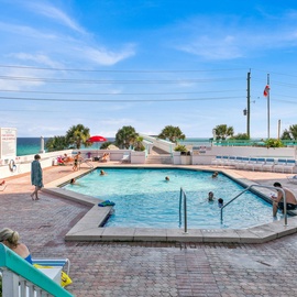 Large pool area with crystal-clear waters and stunning gulf views, surrounded by palm trees and comfortable loungers.