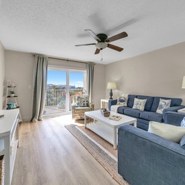 Welcome to Islander Beach Resort 311 - Sandy Dunes! Relax in your bright, coastal living room with comfy blue sofas and refreshing ceiling fan breezes.
