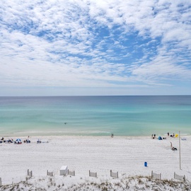 Pristine white sand beach stretches endlessly beneath brilliant blue skies, with crystal-clear turquoise waters perfect for swimming and relaxation.