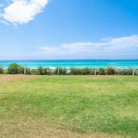 Pristine beachfront property featuring expansive green lawn leading directly to stunning turquoise waters and sandy beach access.