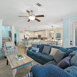 Relax in your spacious living room with plush blue sectional seating, coastal decor, and open kitchen views.