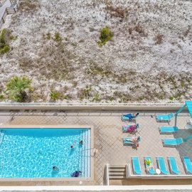 Aerial view of the pool area surrounded by natural dunes and coastal vegetation, with beach access walkway visible.