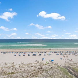 Pristine white sand beach with emerald waters stretches endlessly under brilliant blue skies dotted with fluffy white clouds.