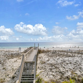 Pristine private beach access with a wooden boardwalk leading to crystal-clear waters under expansive blue skies.