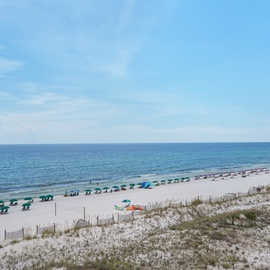Pristine white sand beach stretches along crystal-clear waters with colorful umbrellas and beachgoers enjoying the coastal paradise.