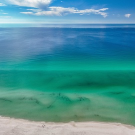 Stunning aerial view showcases pristine emerald waters meeting white sandy shores under brilliant blue skies.