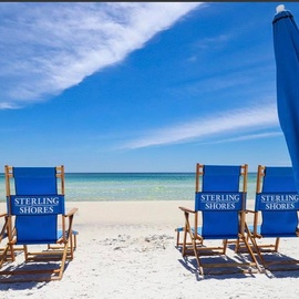 Private beach access with Sterling Shores branded chairs and umbrella overlooking pristine white sand and emerald waters.