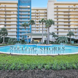 Sterling Shores resort features multi-story beachfront buildings with palm tree landscaping and a decorative entrance fountain.