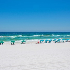 Pristine white sand beach with emerald waters and colorful umbrellas stretching along the coastline under clear blue skies.