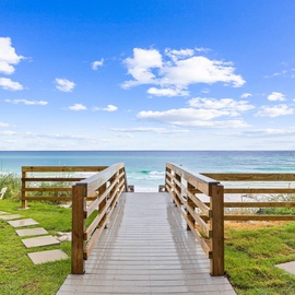 A wooden boardwalk leads through landscaped grounds to pristine beach access with turquoise waters and white sand beyond.