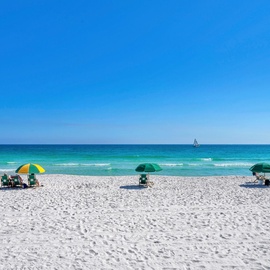 Pristine white sand beach with crystal-clear turquoise waters and colorful umbrellas dotting the shoreline under brilliant blue skies.