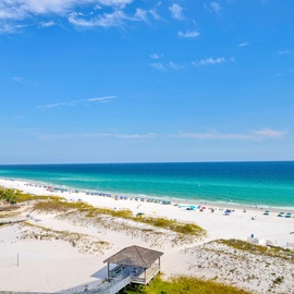 Pristine white sand beach stretches along turquoise waters under brilliant blue skies, with beachfront high-rise building nearby.