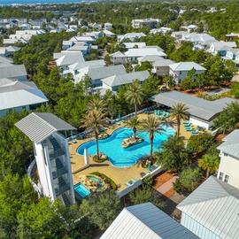 Aerial view of the vacation rental property showcasing the beautiful swimming pool surrounded by palm trees and residential buildings in a peaceful neighborhood setting.