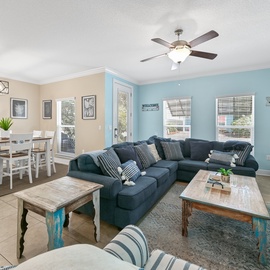 Relax in your coastal-themed living space with comfortable sectional seating and open dining area, perfect for family gatherings.